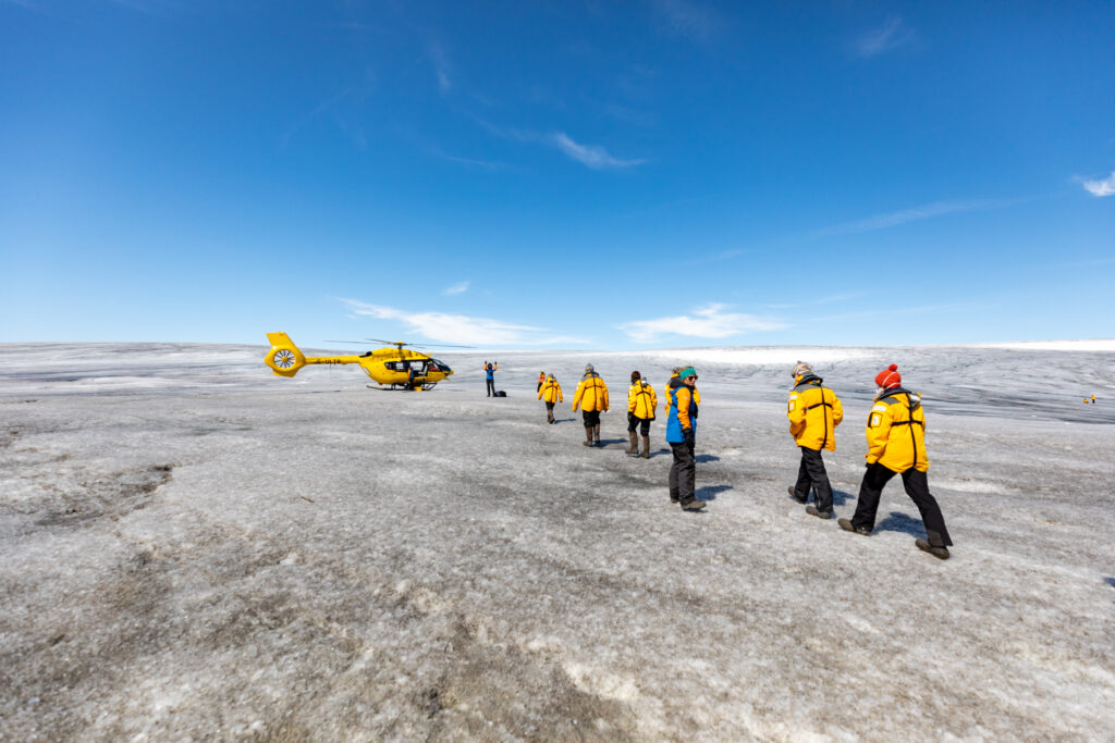 Guests walking on the Greenland ice sheet beside a helicopter